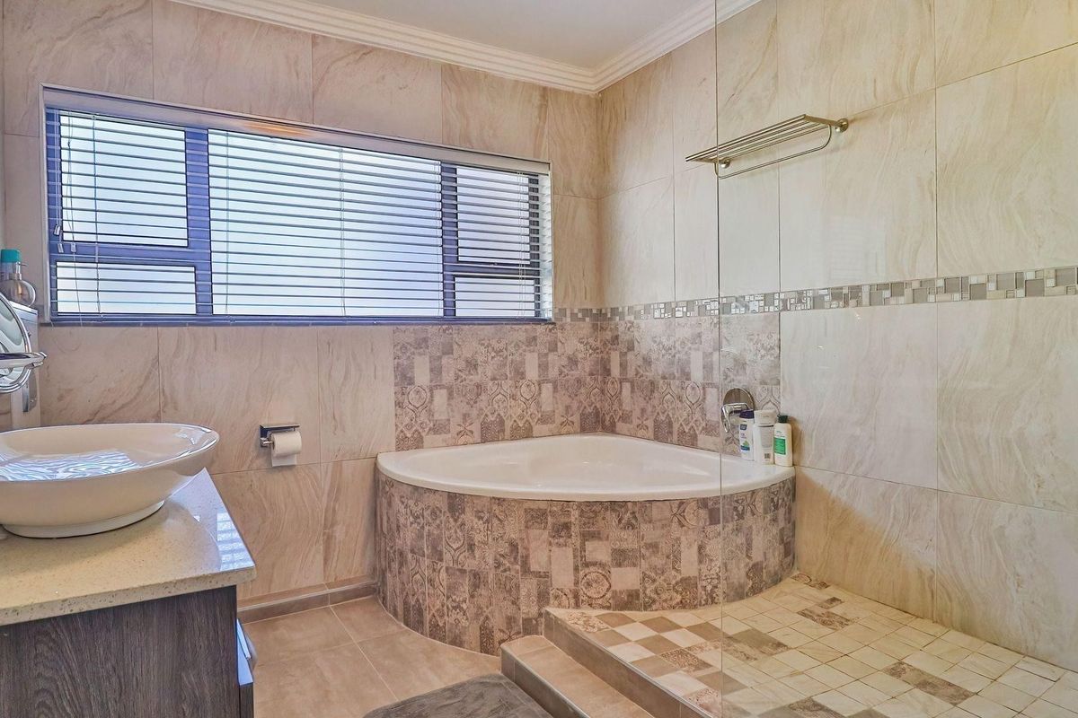 Modern bathroom featuring a corner bathtub, glass shower screen, vessel sink on a stone vanity, and neutral floor-to-ceiling tiling.