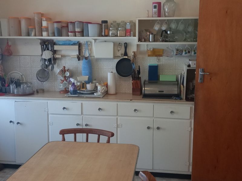 A functional kitchen area featuring white built-in cabinetry, open shelving, and a tiled backsplash, offering potential for a modern cosmetic update.