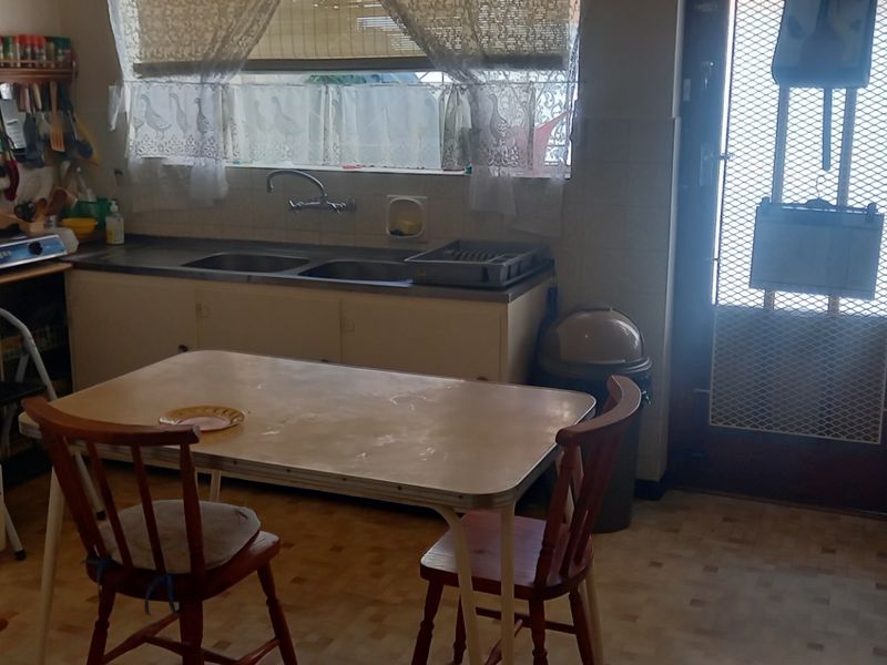 A dated kitchen featuring original cabinetry, a double sink, and a freestanding stove, with direct access to the exterior via a security gate.