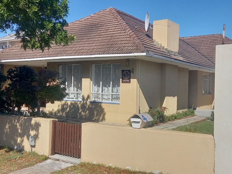 Front elevation of a single-story house featuring a tiled roof, boundary wall with pedestrian gate, and security bars on windows.