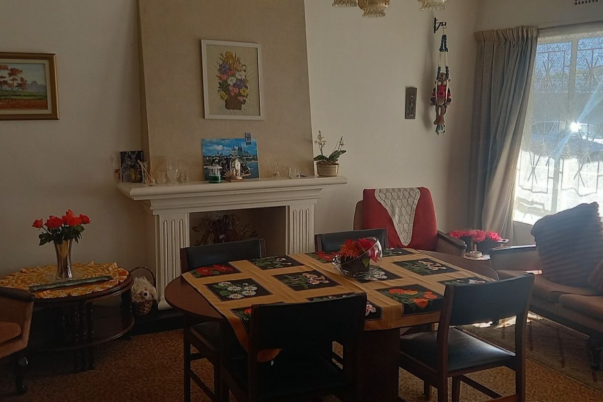 A traditional living room featuring a central fireplace with a decorative mantelpiece and large windows fitted with security gates.