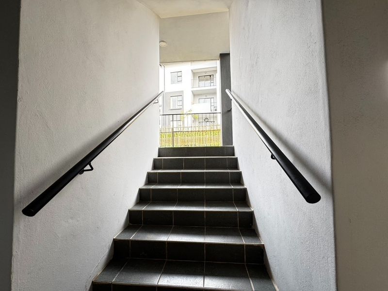 A clean, well-maintained stairwell entrance featuring dark tiled steps and modern black metal handrails leading to an outdoor landing area.