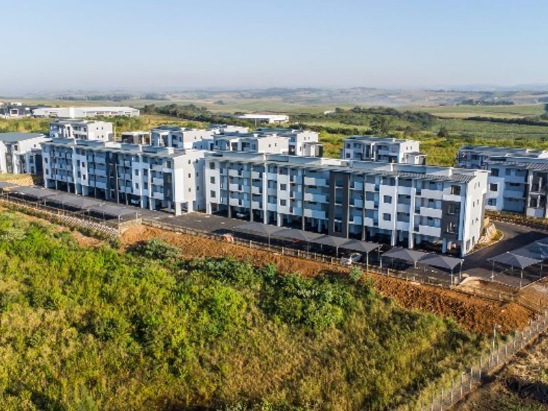 Aerial view of a modern multi-story apartment complex featuring covered parking bays and surrounding landscaped grounds.