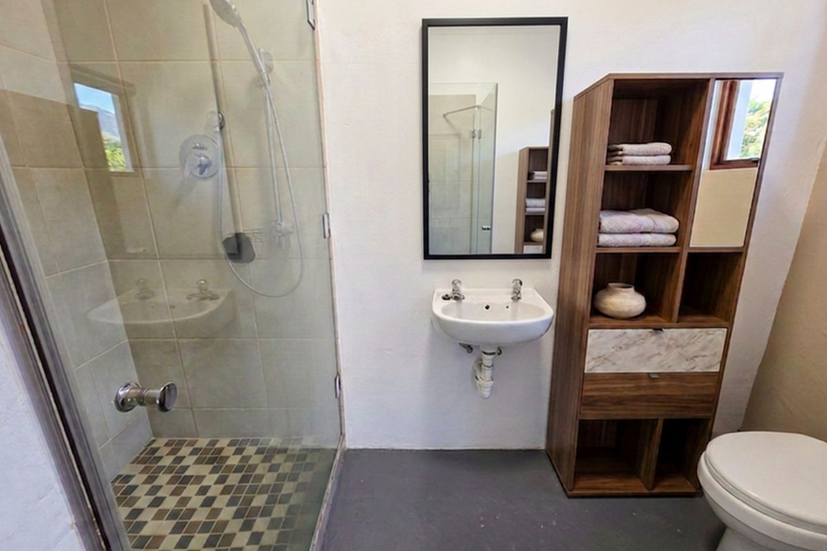 A functional bathroom featuring a glass-enclosed shower, wall-mounted basin, and toilet with modern finishes and neutral tiling.