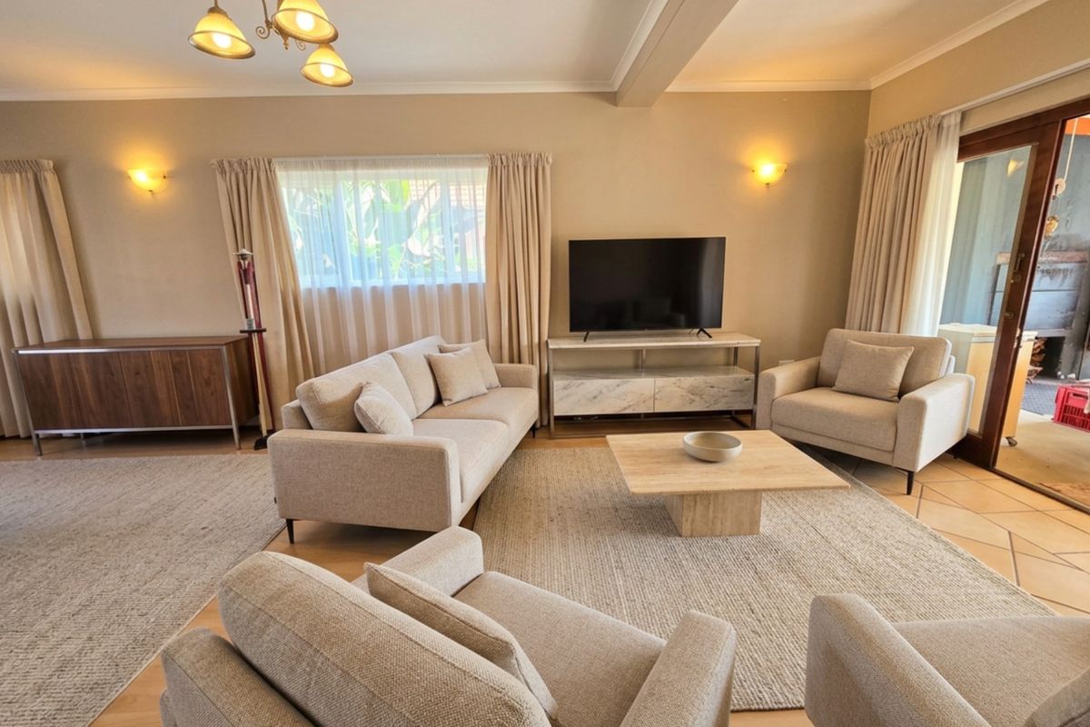 A well-maintained living room featuring a mix of laminate and tiled flooring, wall sconces, and a sliding glass door leading to an outdoor area.