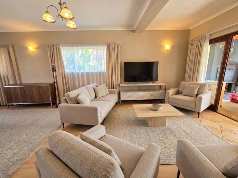 A well-maintained living room featuring a mix of laminate and tiled flooring, wall sconces, and a sliding glass door leading to an outdoor area.