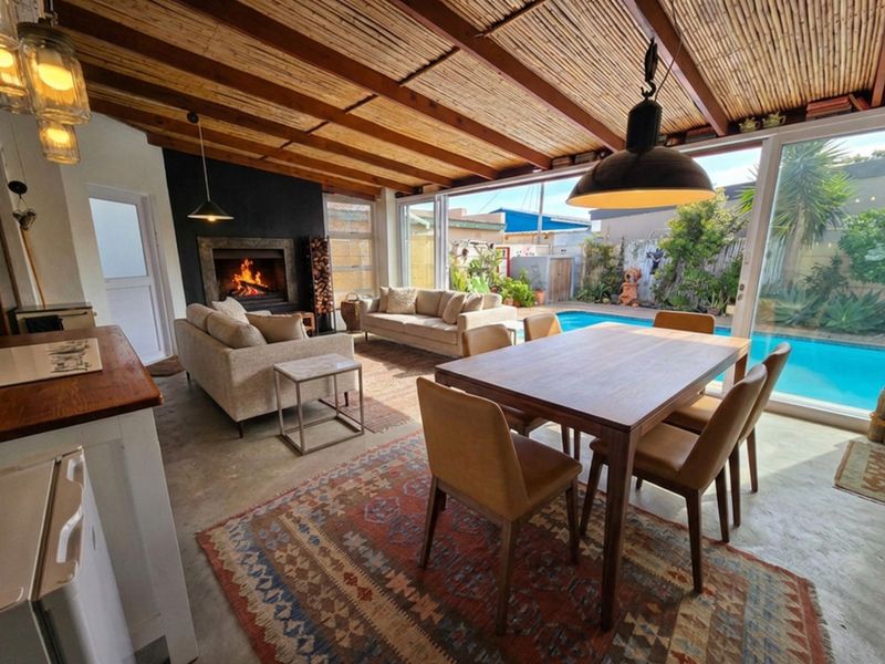 Spacious open-plan living and dining area featuring a fireplace, exposed beam ceiling, and large sliding doors opening to a swimming pool.