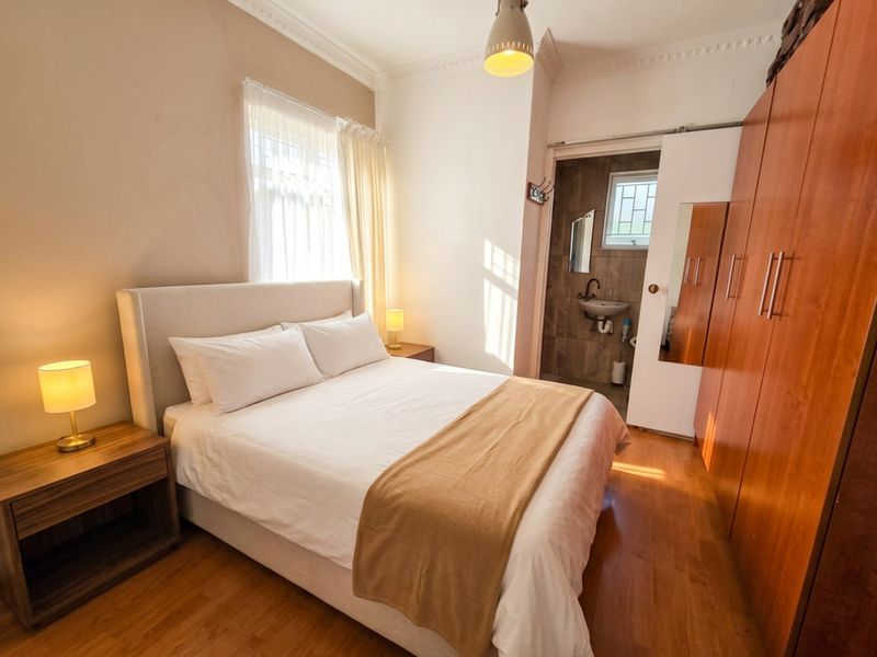 A well-maintained bedroom featuring laminate flooring, built-in cupboards, and an adjoining en-suite bathroom with tiled finishes.