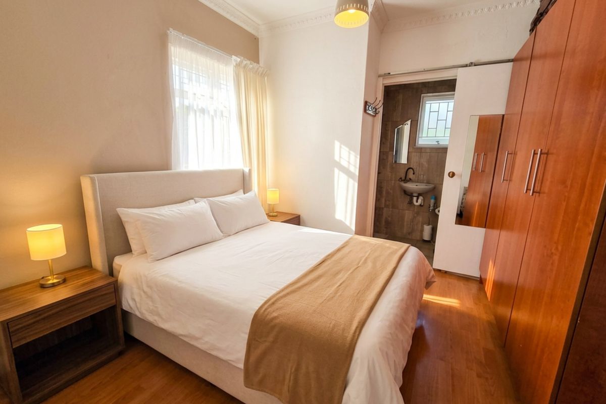 A well-maintained bedroom featuring laminate flooring, built-in cupboards, and an adjoining en-suite bathroom with tiled finishes.