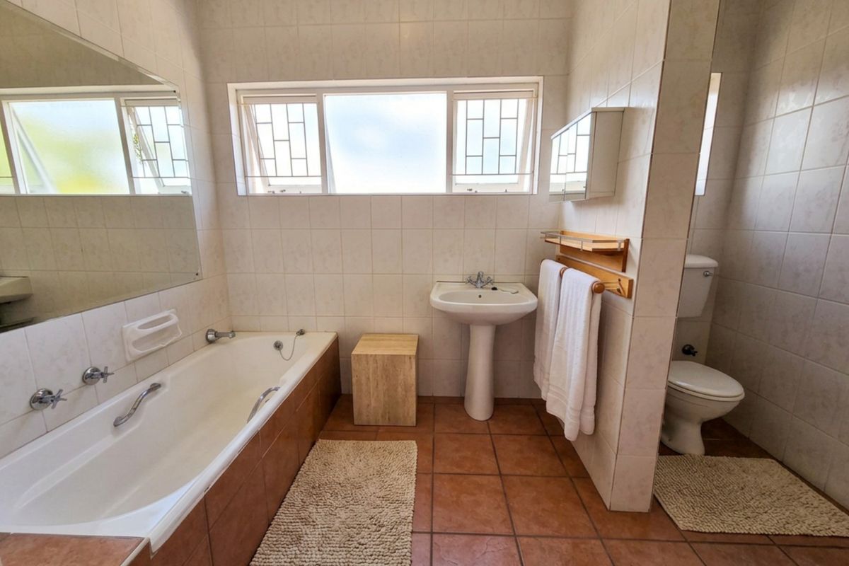 A functional bathroom featuring a built-in bathtub, pedestal sink, and a separate toilet area with tiled finishes throughout.