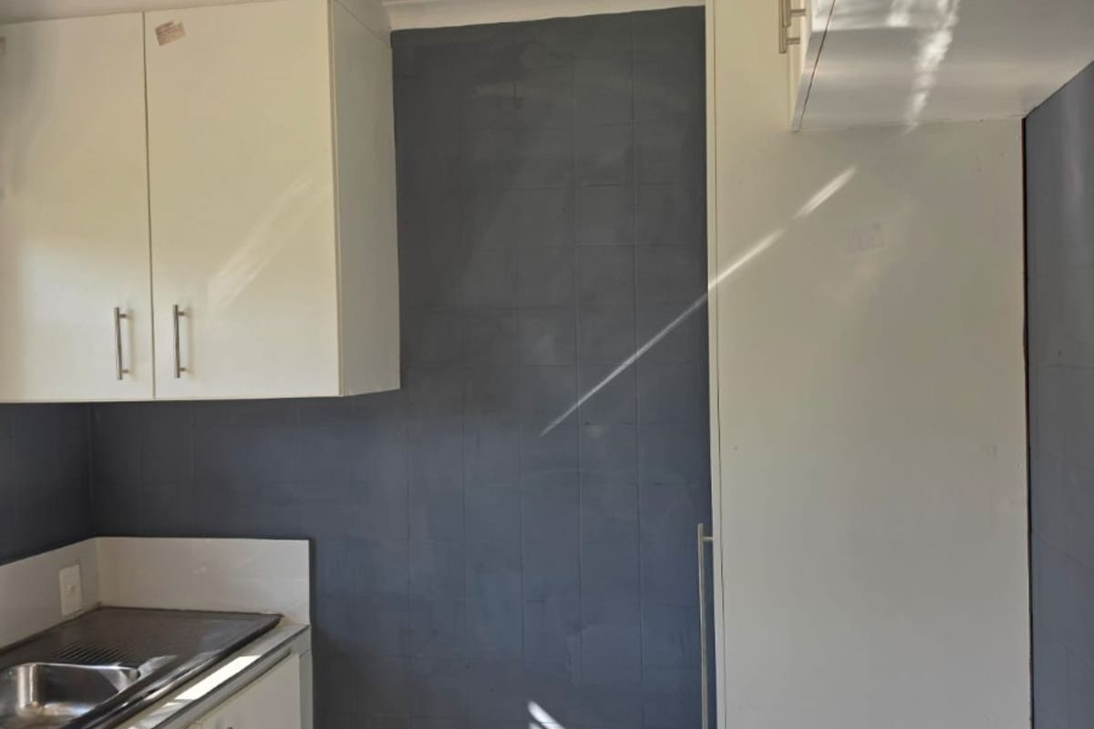 A compact kitchen area featuring white built-in cabinetry, a stainless steel sink, and a dark tiled splashback.