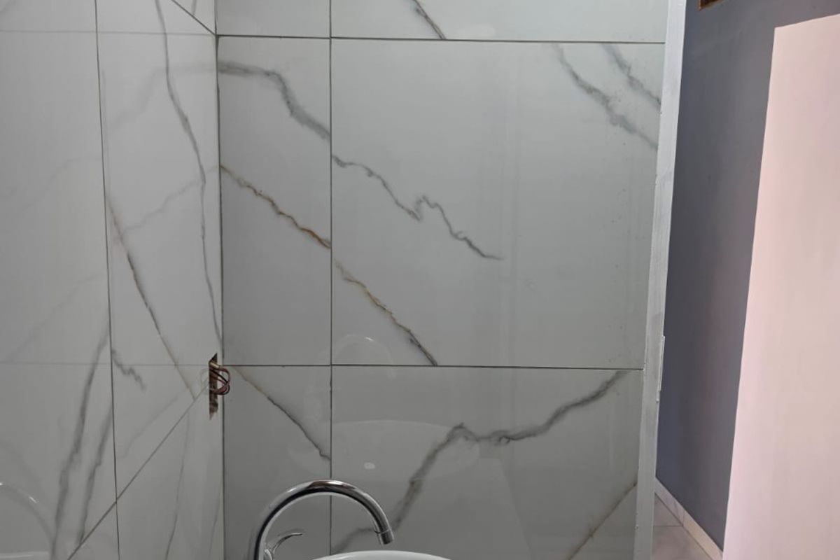 A modern bathroom vanity area featuring a white vessel sink, chrome faucet, and elegant marble-look wall tiles, currently awaiting final finishing touches.