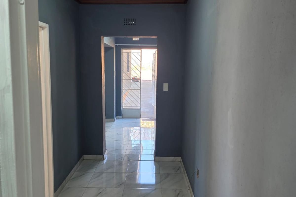A bright hallway featuring marble-look floor tiles and a timber ceiling, leading towards an exterior security gate.