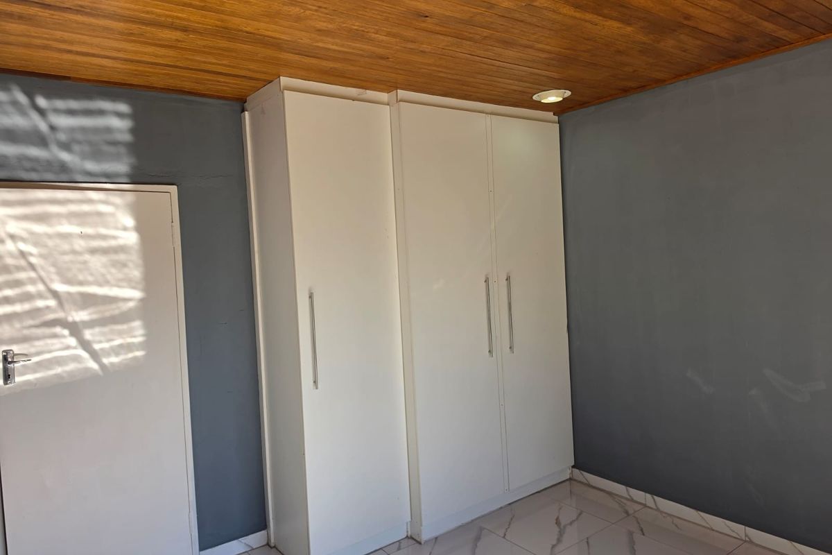 A clean bedroom featuring built-in cupboards, a warm timber ceiling, and modern tiled flooring.