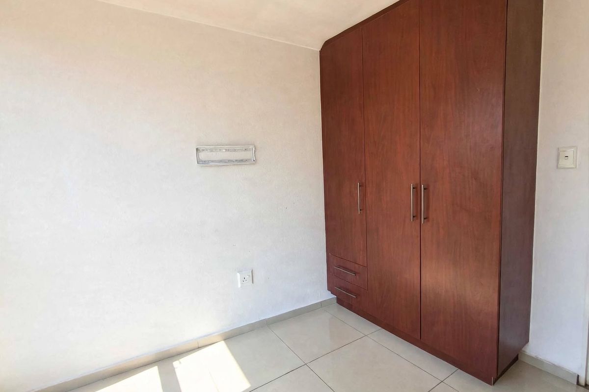 A clean, empty bedroom featuring neutral tiled flooring and a large, dark wood built-in wardrobe with ample storage space.