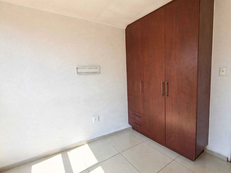 A clean, empty bedroom featuring neutral tiled flooring and a large, dark wood built-in wardrobe with ample storage space.