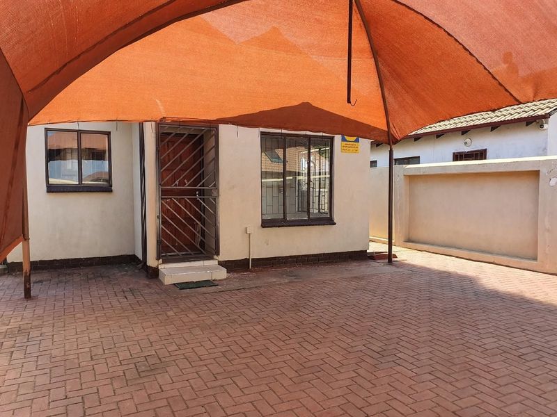 Rear exterior area featuring a paved courtyard, security gate, and a large shade sail providing covered outdoor space.