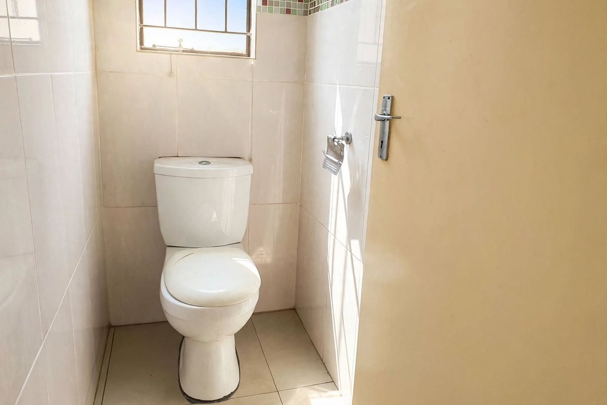A compact, functional bathroom featuring tiled walls and flooring, a standard toilet, and a window with security bars.