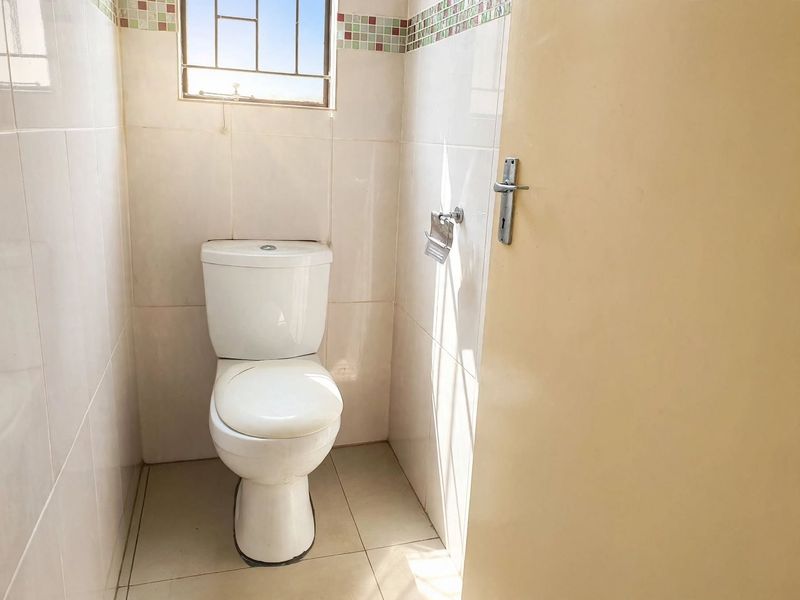 A compact, functional bathroom featuring tiled walls and flooring, a standard toilet, and a window with security bars.