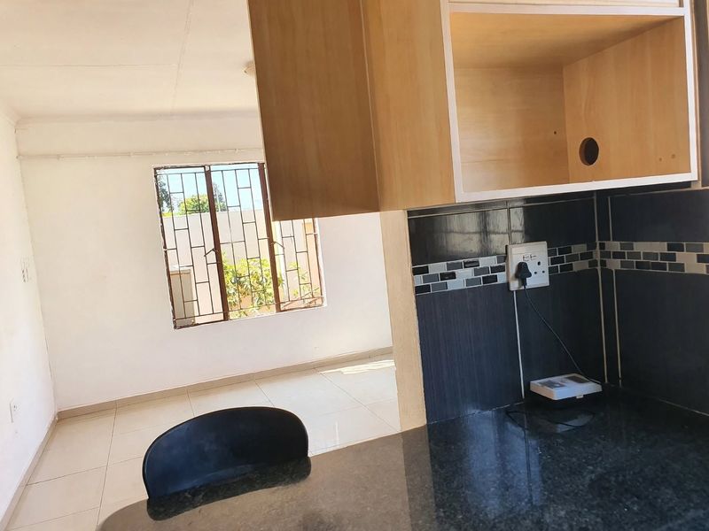 A functional kitchen area featuring granite countertops, tiled backsplash, and built-in cabinetry, with an open view into the adjacent living space.