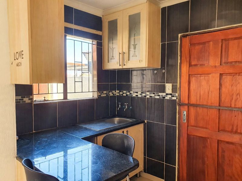 A compact kitchen featuring dark tiled walls, granite countertops, built-in cabinetry, and a wooden door leading to the exterior.
