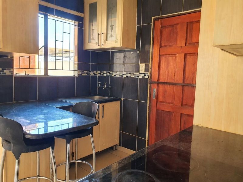 Compact kitchen featuring dark tiled walls, granite countertops, built-in cabinetry, and a functional hob, providing a practical workspace.