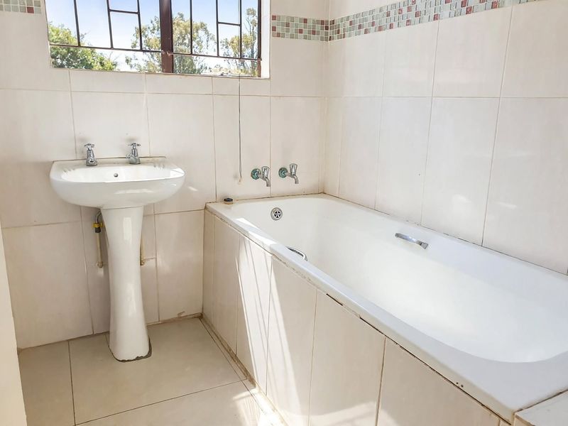 A functional bathroom featuring a white pedestal basin, a built-in bathtub, and neutral wall tiling with a decorative mosaic border.