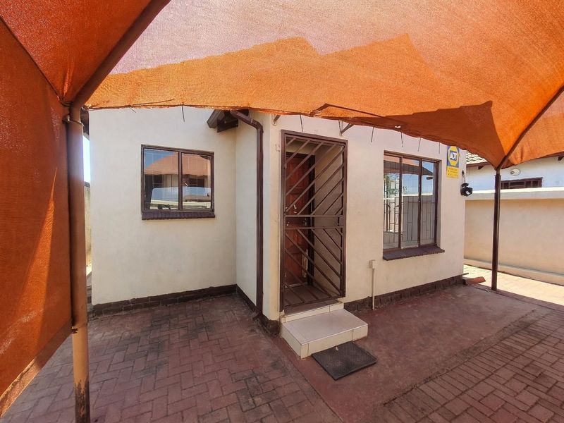 Rear exterior view featuring a paved patio area covered by a shade sail, with a secure entrance door and window security bars.