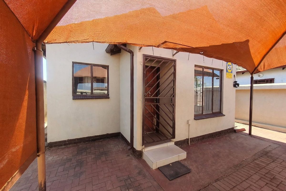 Rear exterior view featuring a paved patio area covered by a shade sail, with a secure entrance door and window security bars.