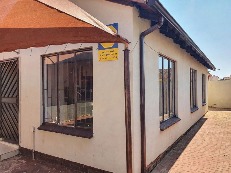 Rear exterior view of the property featuring paved walkways, security bars on windows, and installed guttering and downpipes.