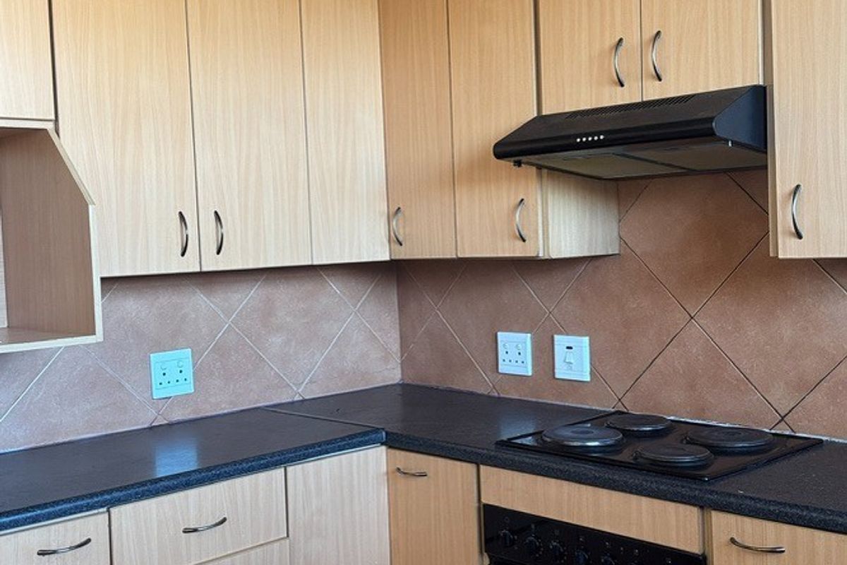 A functional kitchen featuring light wood-finish cabinetry, dark countertops, a built-in oven with hob, and a tiled backsplash.