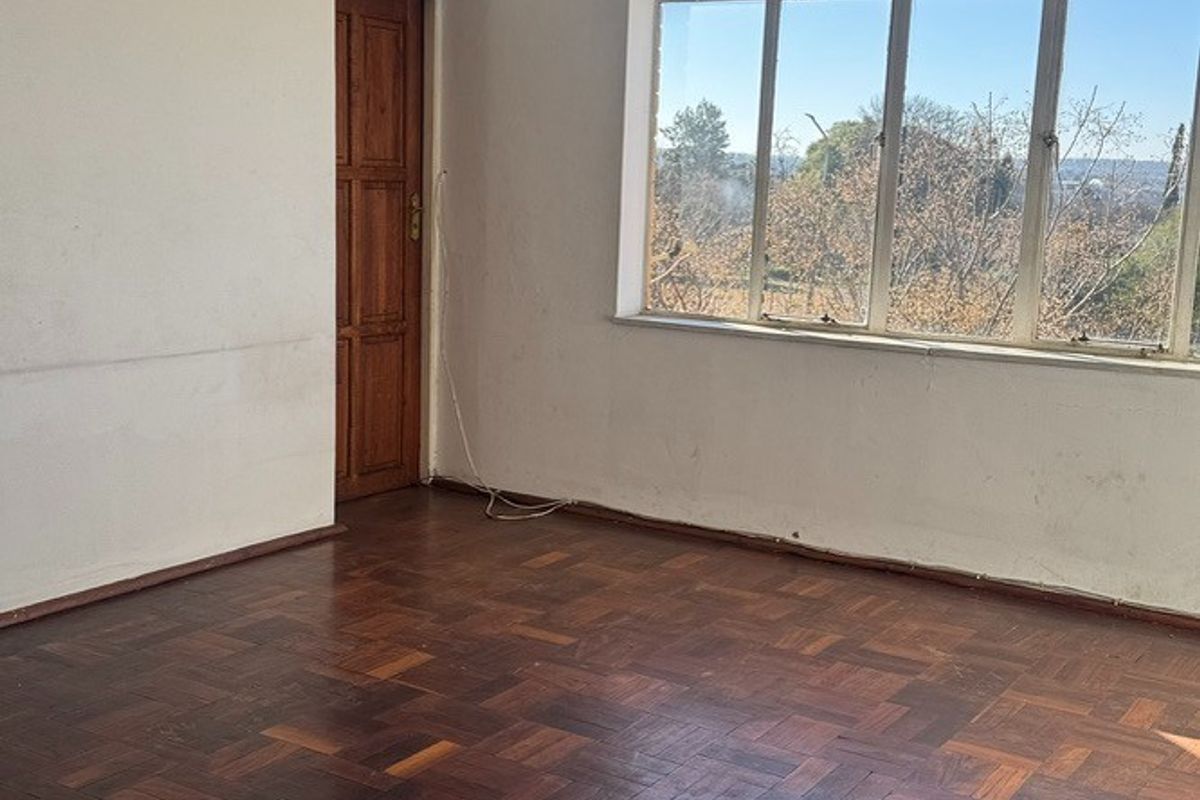 An empty living room featuring classic parquet flooring, a large window with natural light, and a wooden door.