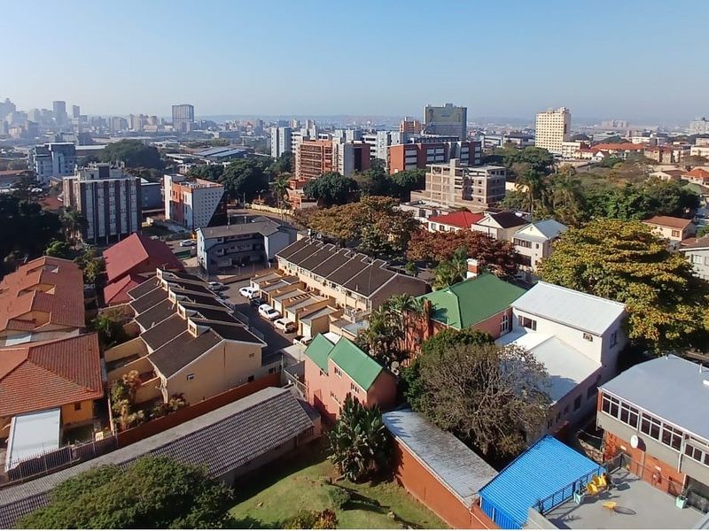 An elevated aerial view showcasing the surrounding urban neighborhood, residential apartment complexes, and city skyline in the distance.