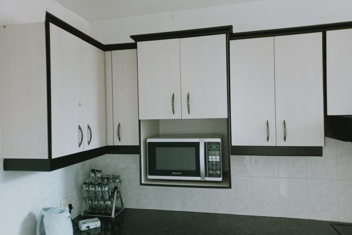 A functional kitchen area featuring white cabinetry with dark trim, granite countertops, and a tiled backsplash with a built-in microwave.