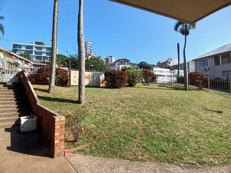 A communal garden area featuring a brick retaining wall, concrete staircase, and metal perimeter fencing within an apartment complex setting.