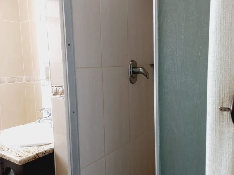 A functional bathroom featuring a tiled shower enclosure, a vanity cabinet with a granite countertop, and a basin with a mixer tap.