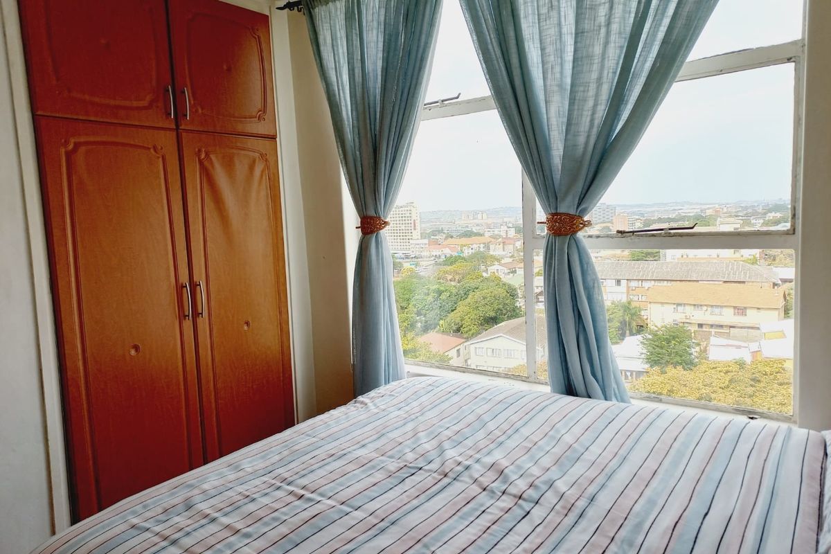 A bedroom featuring a built-in wooden wardrobe and a large window offering an elevated urban view.