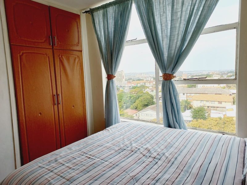 A bedroom featuring a built-in wooden wardrobe and a large window offering an elevated urban view.