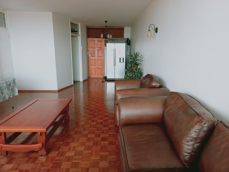 Spacious living area featuring classic parquet flooring, neutral walls, and a solid wood entrance door, offering a functional and well-lit living space.
