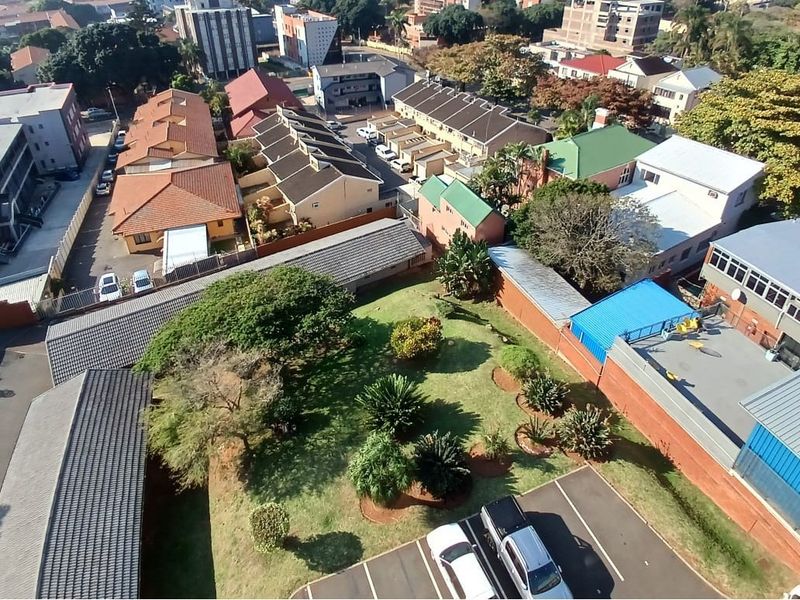 An aerial view of the apartment complex grounds, featuring a central garden area, paved parking bays, and surrounding residential buildings.