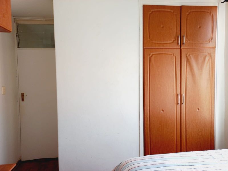 A bedroom interior featuring a built-in wooden wardrobe and a standard internal door with a transom window above.
