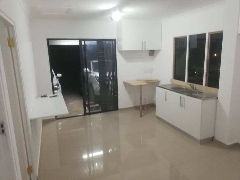 A compact, empty kitchen area featuring white cabinetry, a stainless steel sink, tiled flooring, and a sliding door leading to an exterior space.