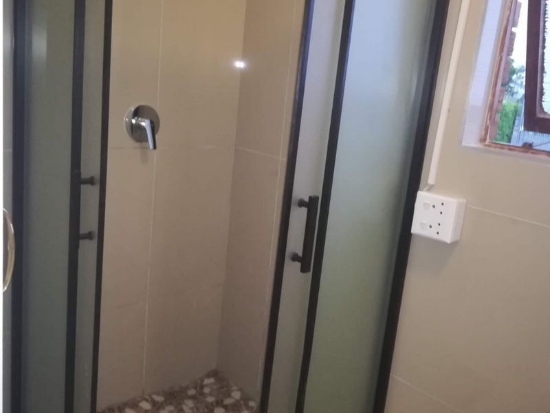 A modern bathroom featuring a corner shower enclosure with a black frame, tiled walls, and a pebble-style shower floor.