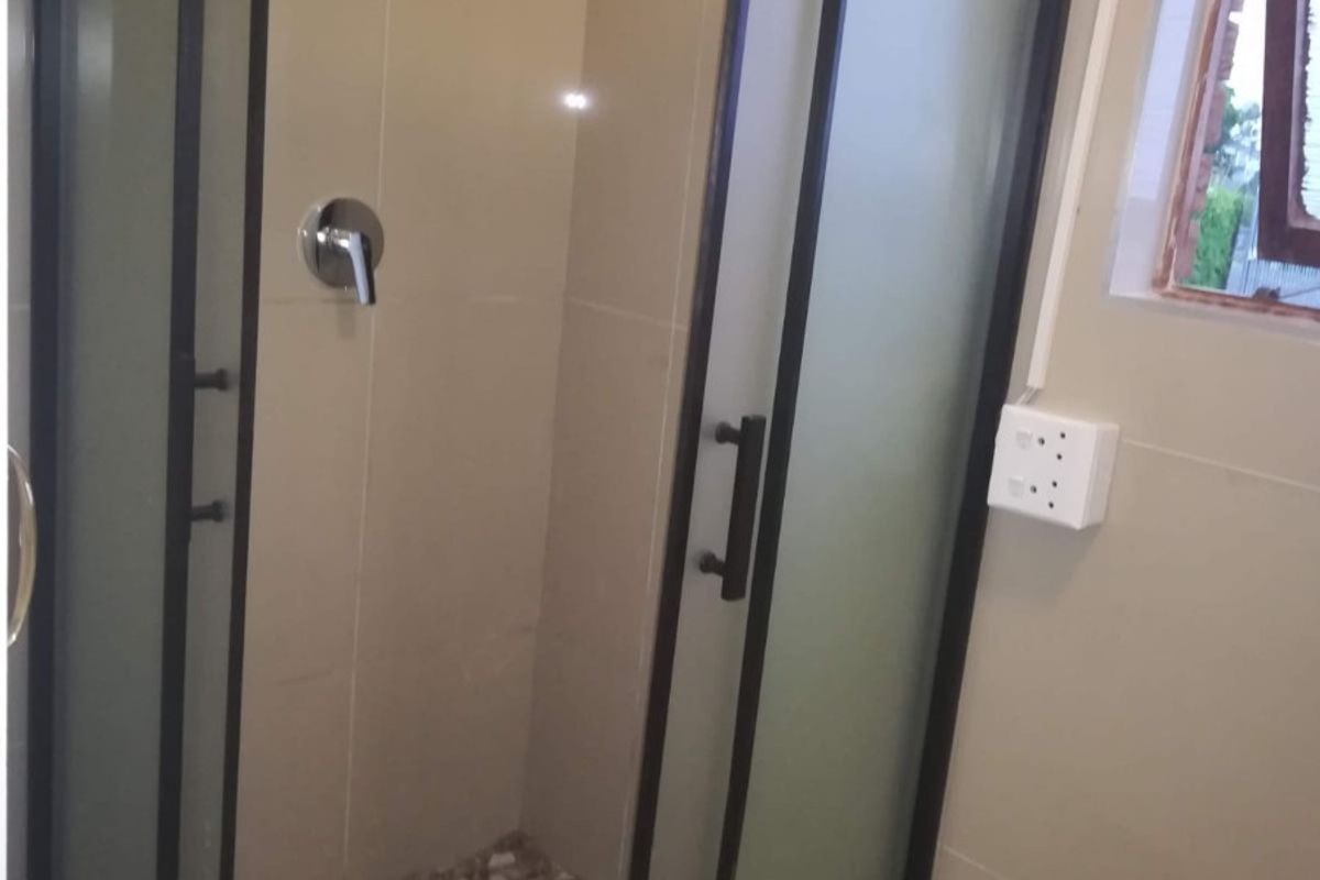 A modern bathroom featuring a corner shower enclosure with a black frame, tiled walls, and a pebble-style shower floor.