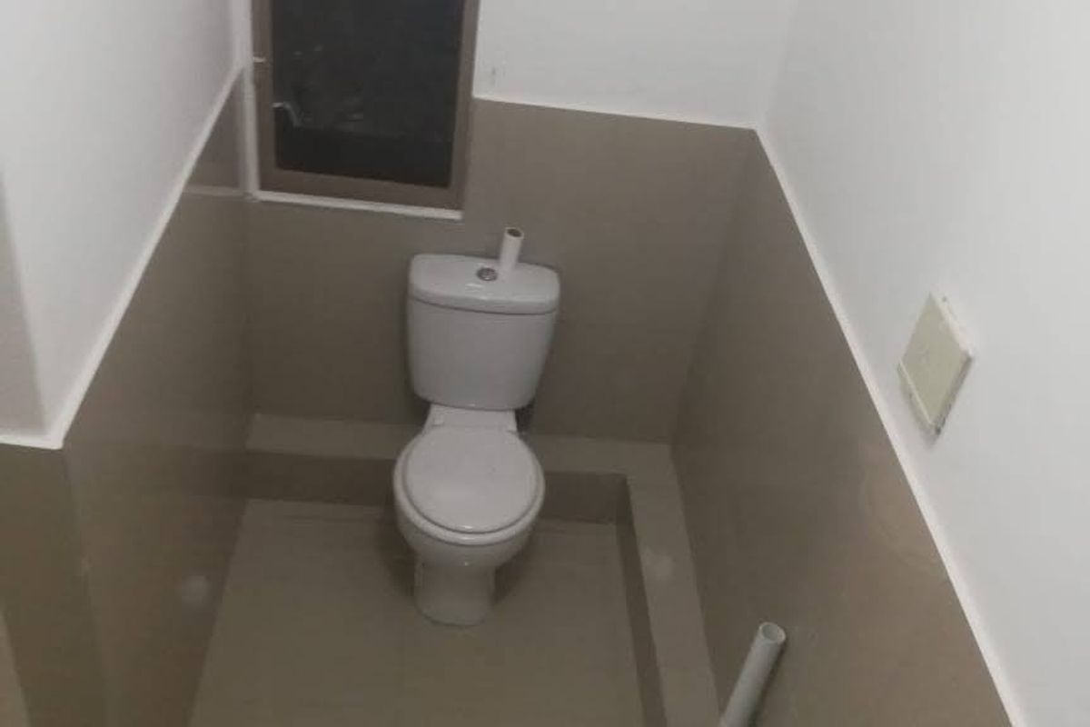 A compact bathroom featuring a pedestal basin, toilet, and neutral tiled wall cladding with a small window for natural light.