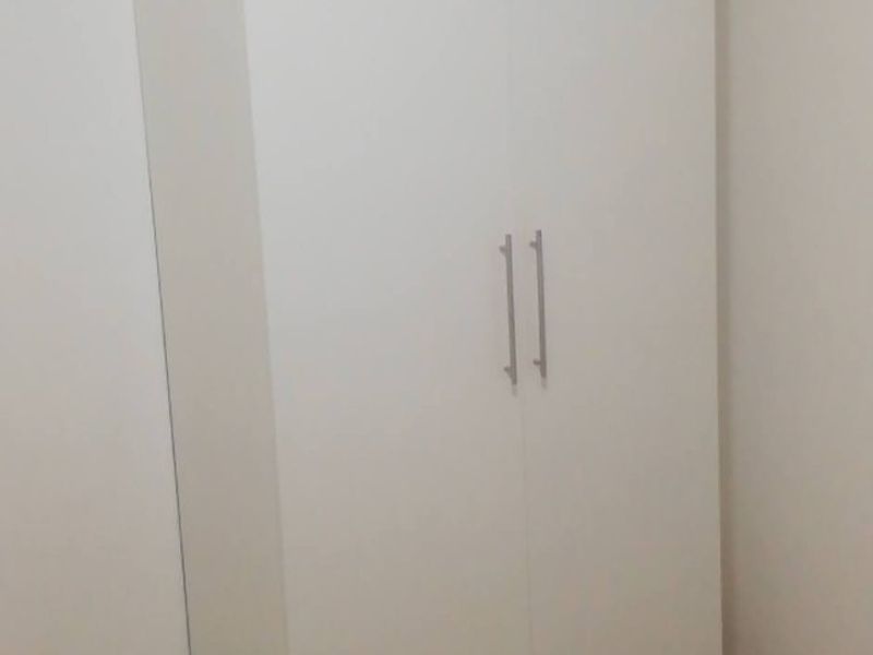 A clean, minimalist bedroom featuring a modern white built-in wardrobe with sleek metal handles, offering ample storage space.