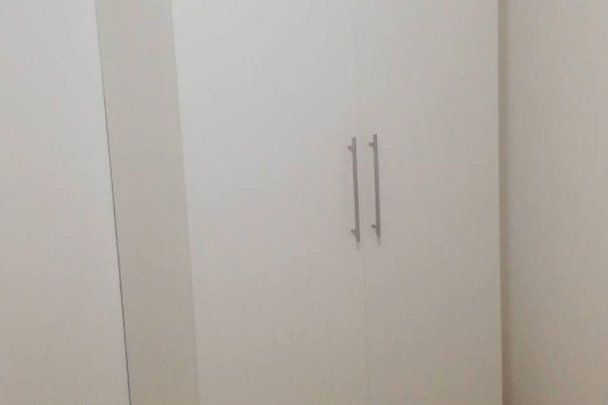 A clean, minimalist bedroom featuring a modern white built-in wardrobe with sleek metal handles, offering ample storage space.