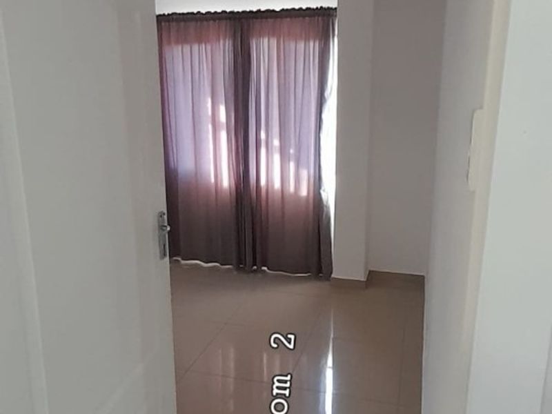 A bright, empty bedroom featuring neutral tiled flooring and curtain tracks, offering a clean canvas for personalization.