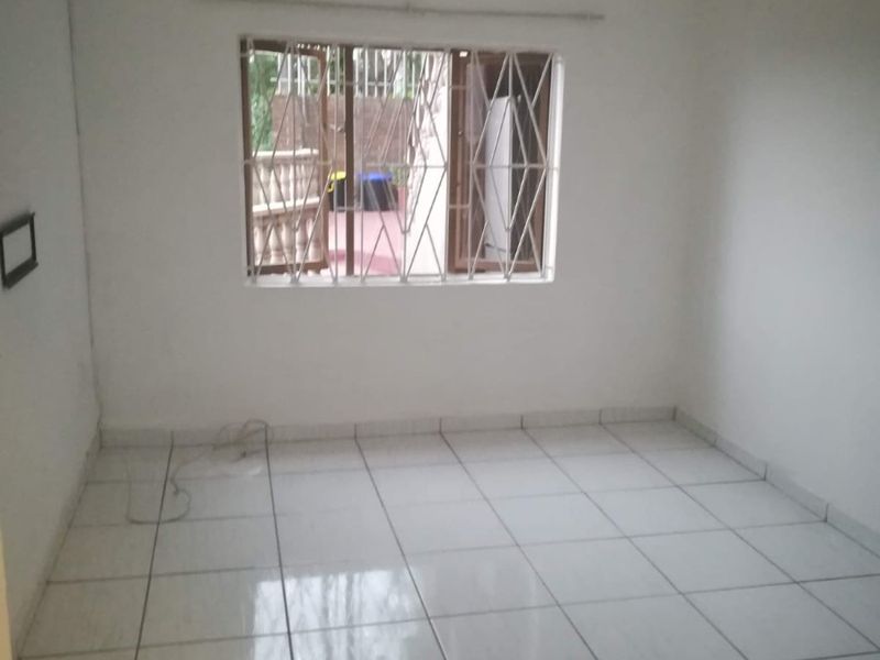 An empty bedroom featuring white tiled flooring, a window with security bars, and a simple ceiling light fixture.