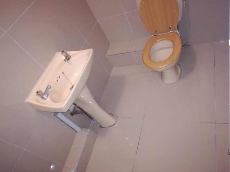 A compact bathroom featuring a pedestal basin and a standard ceramic toilet with tiled walls and flooring throughout.